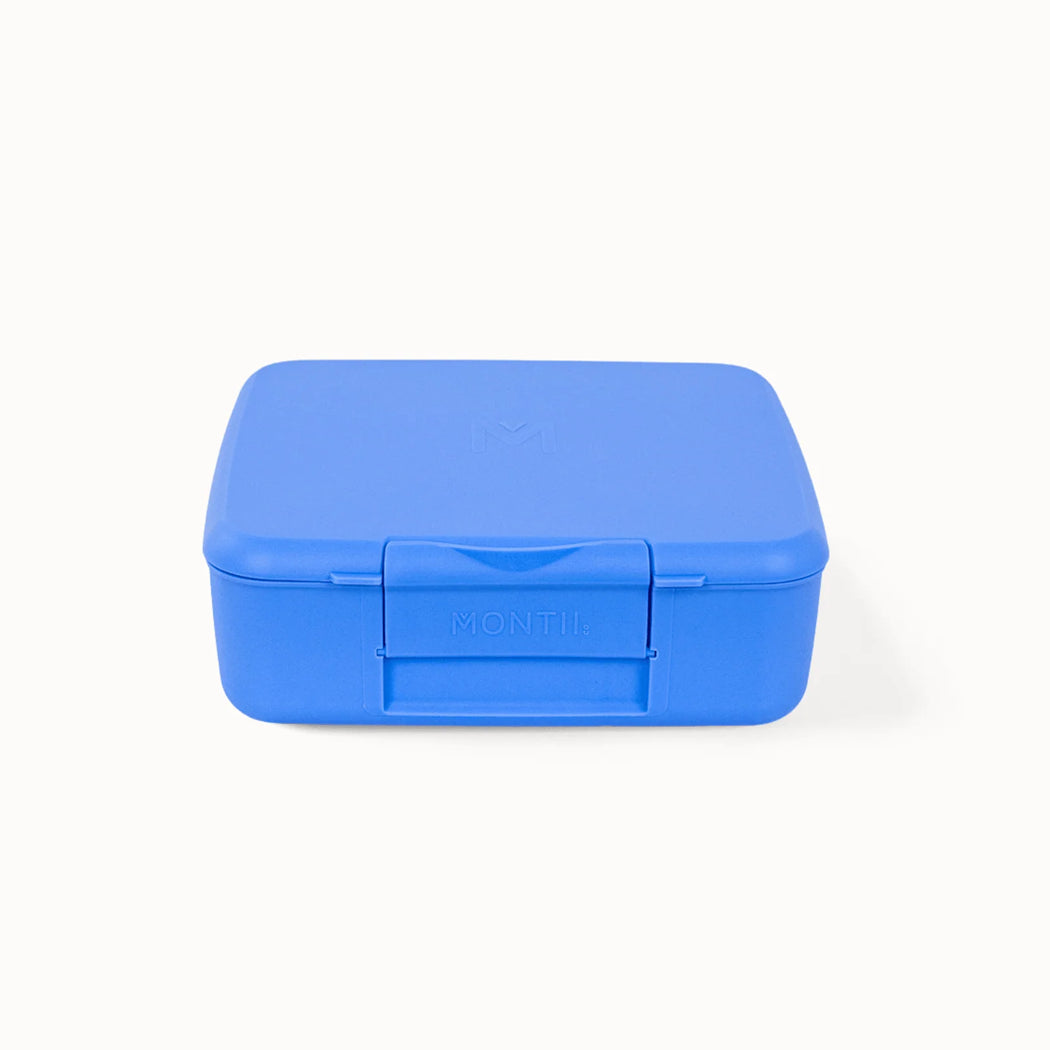 A bright blue Montii plastic lunch box with a secure latched lid, shown from a front-facing perspective on a clean white background.