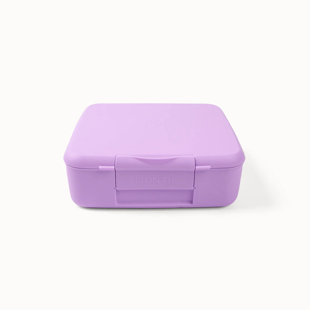 A light purple plastic lunch box with a hinged lid and a front latch, featuring the brand name 'MONTII' embossed on the latch, set against a plain white background.
