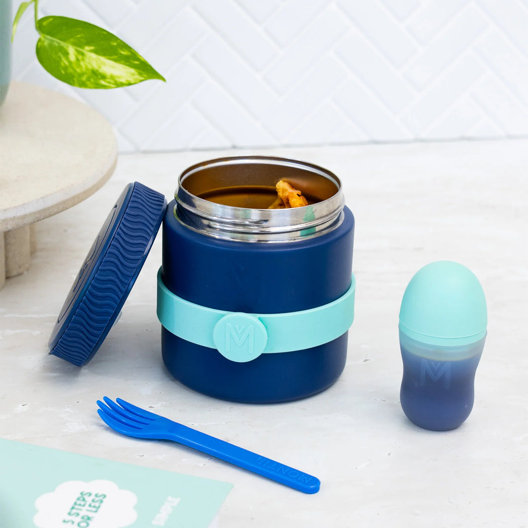 Navy blue food jar with a turquoise band, fork, and small container on a light surface.