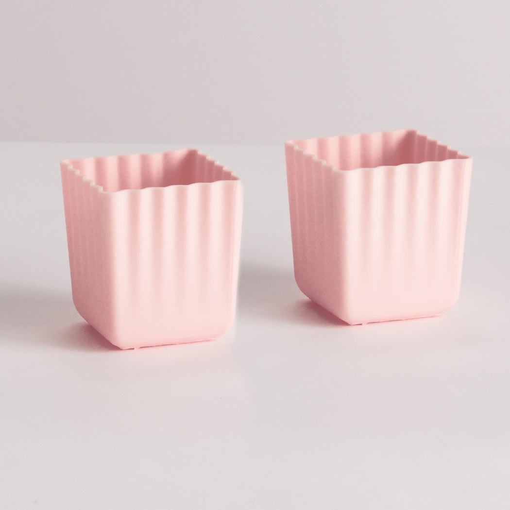 Two small pink square silicone mold cups with fluted edges, shown on a light gray background.