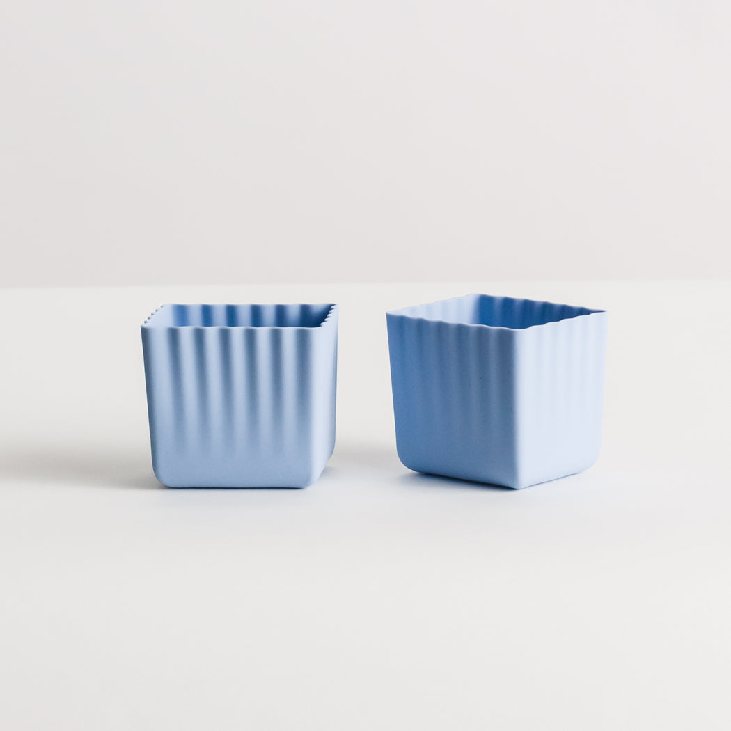 Two small square silicone pots with a fluted vertical rib design, shown in light blue on a clean white background.