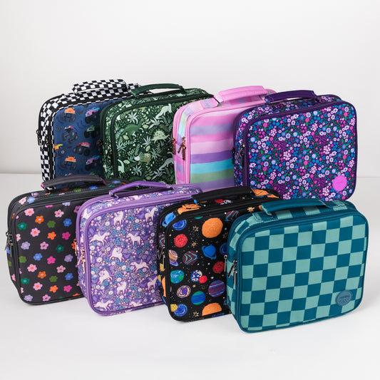 A group of eight patterned lunch bags arranged together on a light gray studio background. The bags feature various designs including floral prints, animal motifs, planets, checkers, stripes, and solid colors.