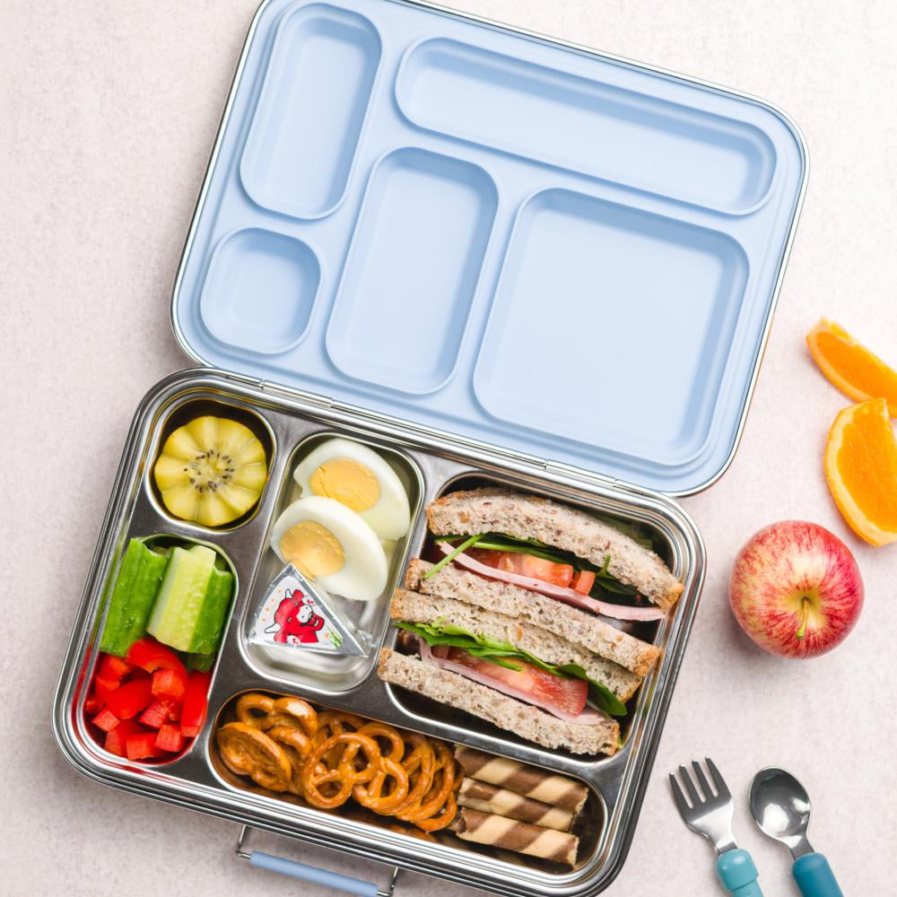 Bento box with a sandwich, fruits, and vegetables on a light surface.