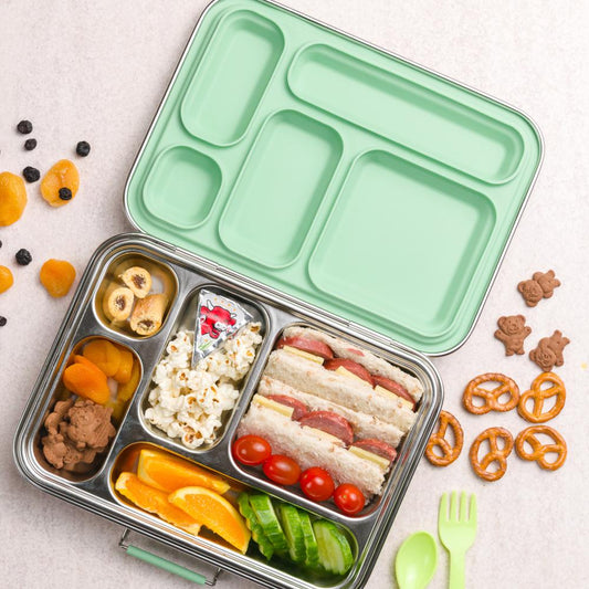 Green bento box with compartments filled with food on a light surface.
