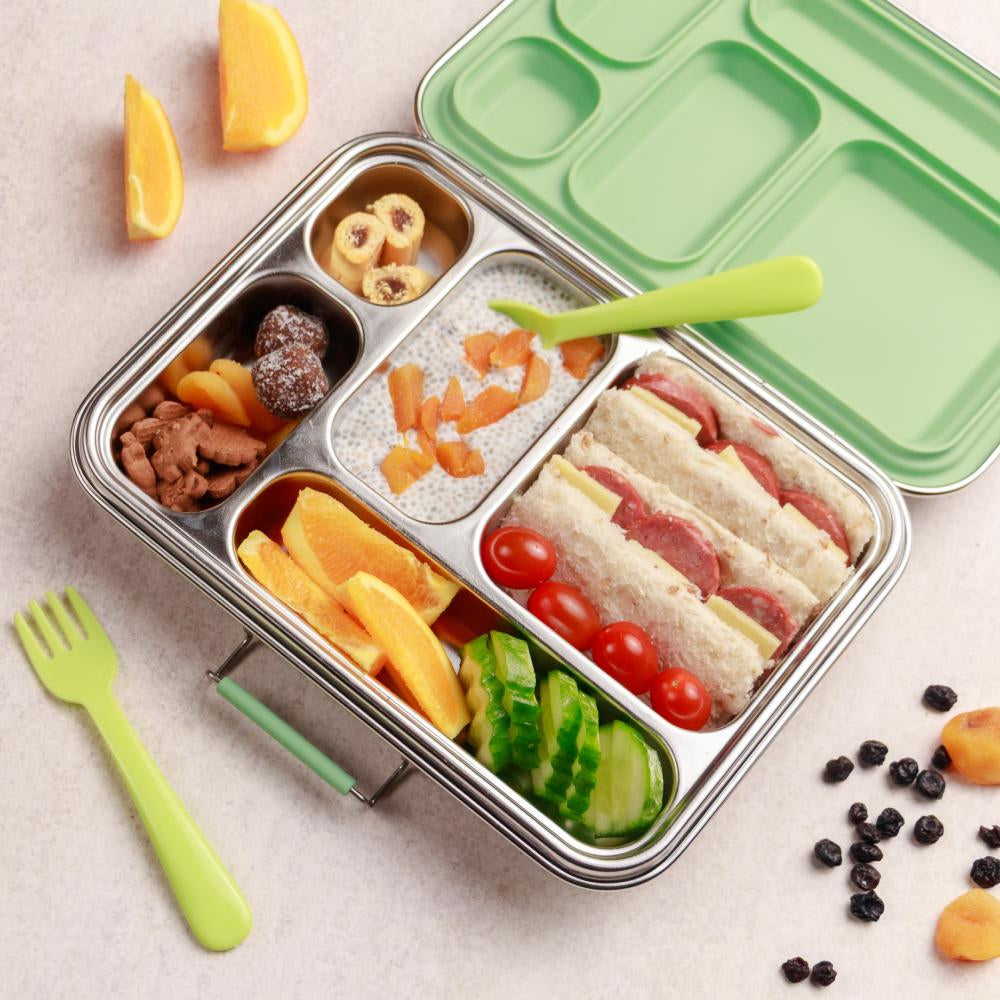 Metal lunch box with compartments containing a sandwich, fruit, and vegetables, with a green lid and fork on a light background.