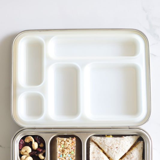 Meal prep container with compartments containing a sandwich, nuts, and other snacks on a white background