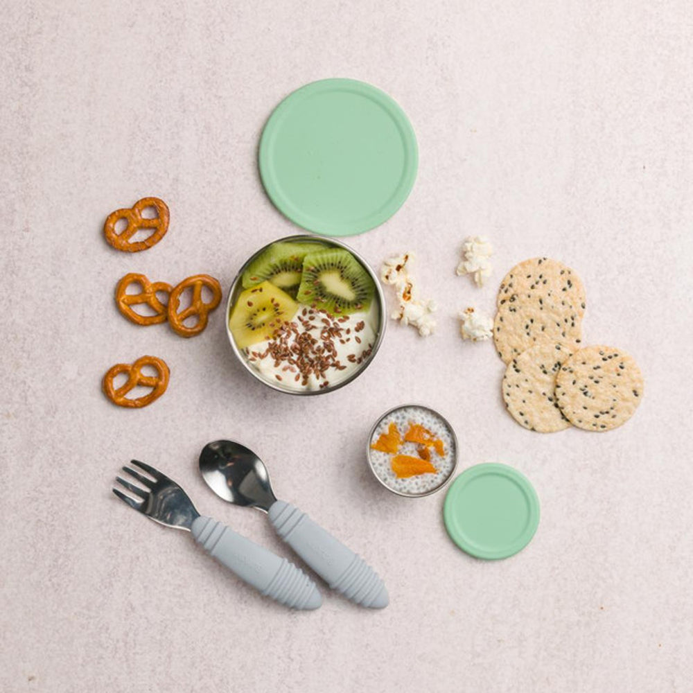Children's tableware set with bowls, utensils, and snacks on a light surface