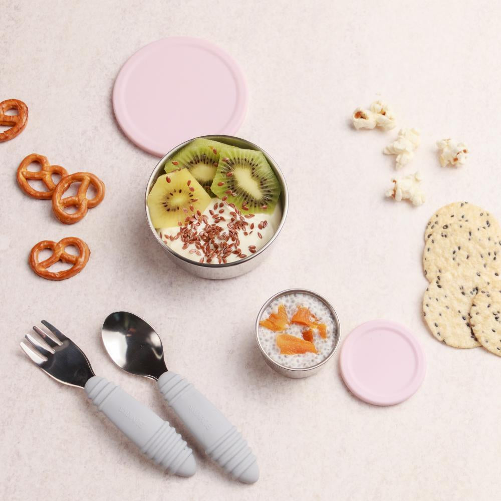 Children's cutlery set with pink handles on a light surface with snacks