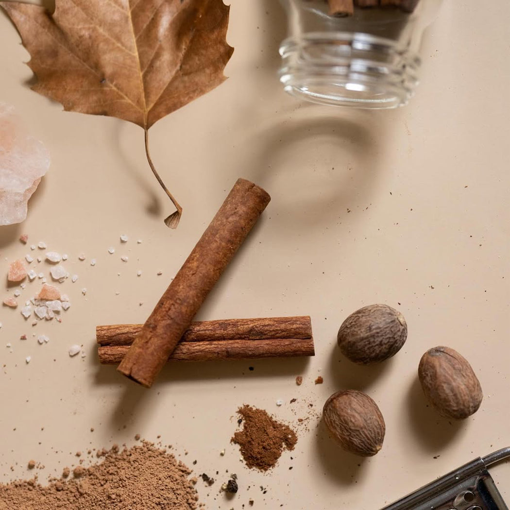 Cinnamon sticks, nutmeg, and ground cinnamon on a beige surface with a glass container.