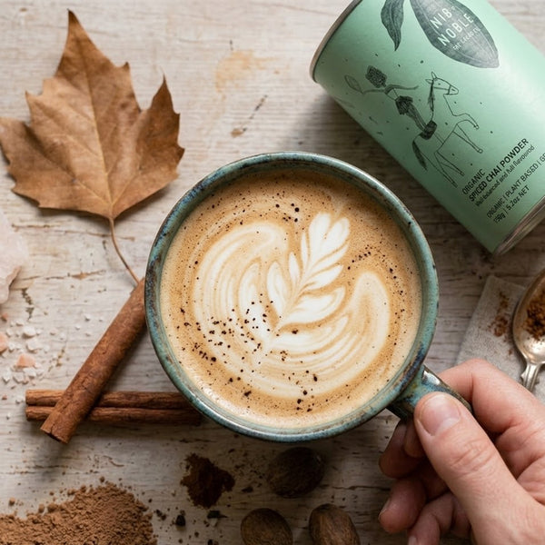 Cup of chai tea with latte art, cinnamon sticks, and a can of organic product on a wooden surface.