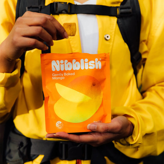 Person holding a Nibblish Gently Baked Mango snack package in a yellow jacket.