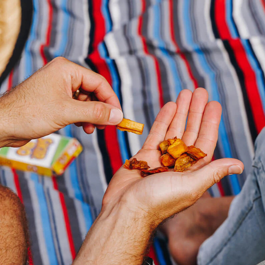 Person holding a small packet of snacks above another person's hand with snacks already in it, against a colorful striped background.
