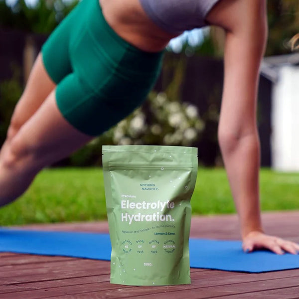Person in green athletic wear stretching outdoors with a packet of Electrolyte Hydration on a wooden surface.