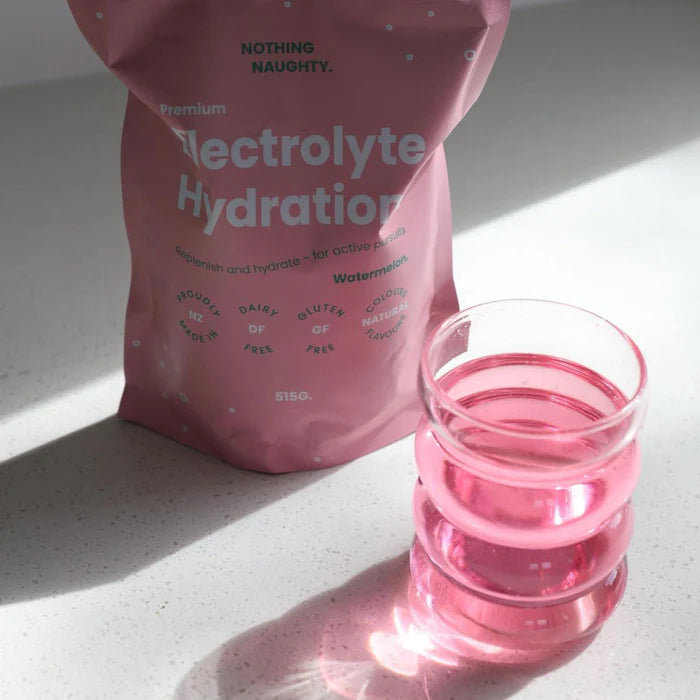 Pink electrolyte hydration package with a glass of pink liquid on a light surface.