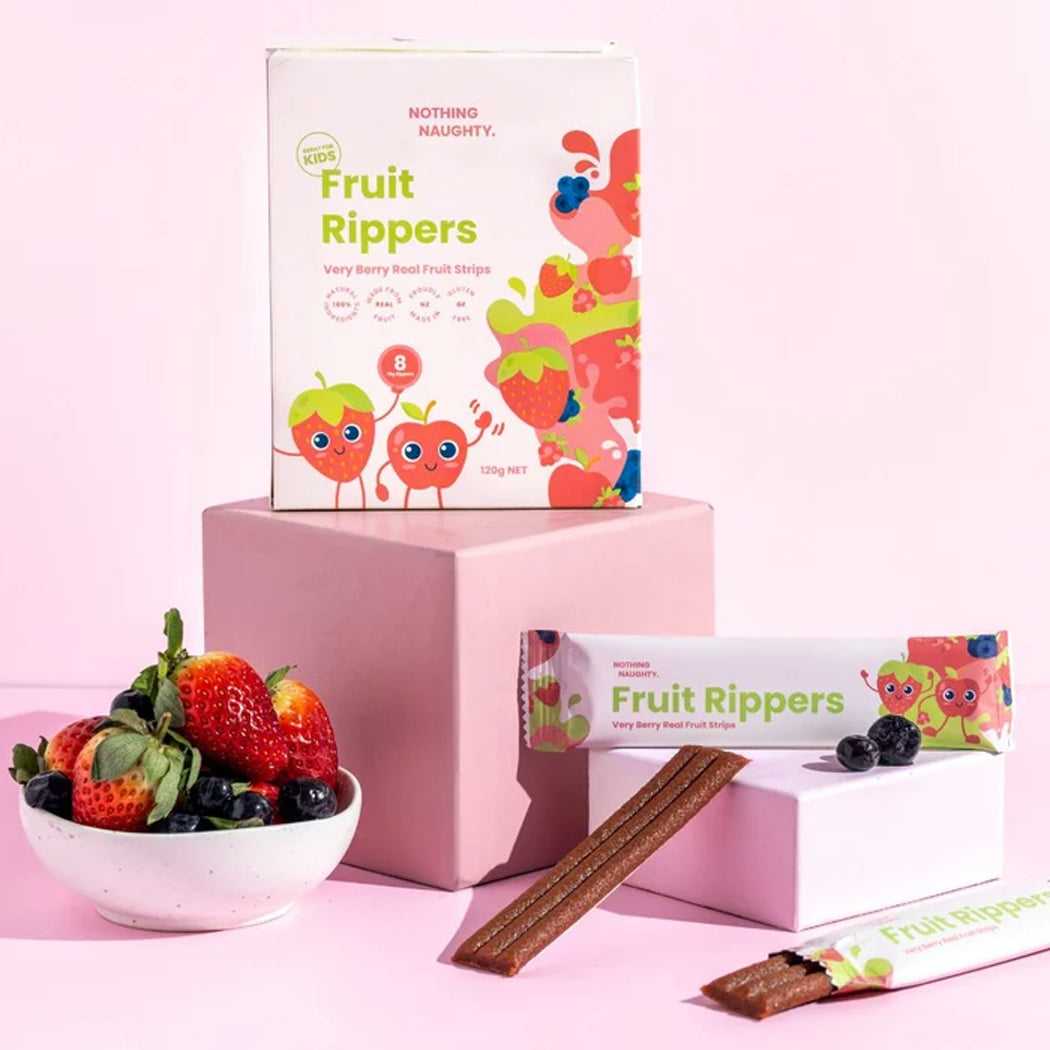 Fruit Rippers very berry seed fruit strips shown with their colorful packaging boxes and a bowl of fresh strawberries and blueberries on a pink background.