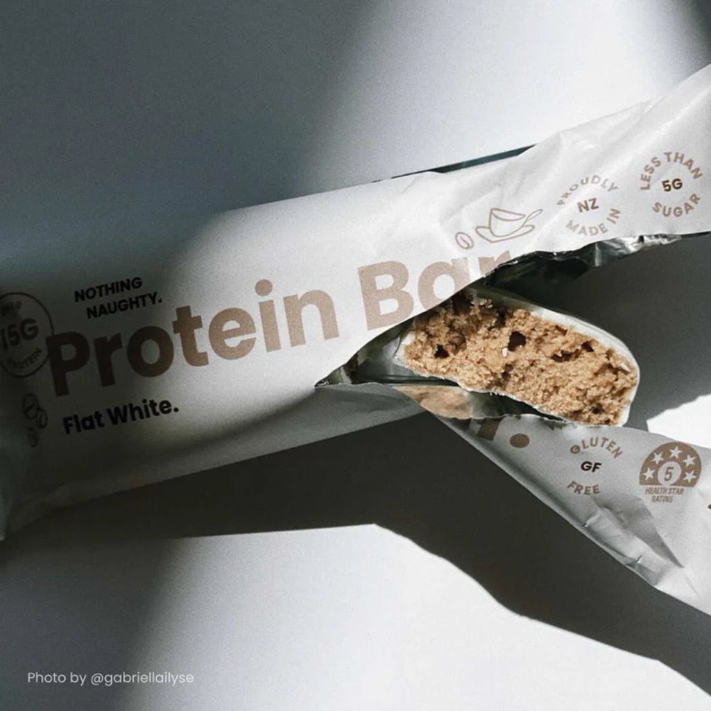 Protein bar with 'Flat White' flavor partially unwrapped, showing the texture inside.