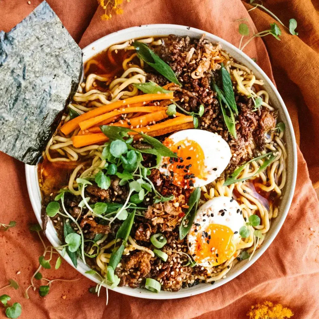 Bowl of ramen with noodles, vegetables, and eggs on a textured orange surface