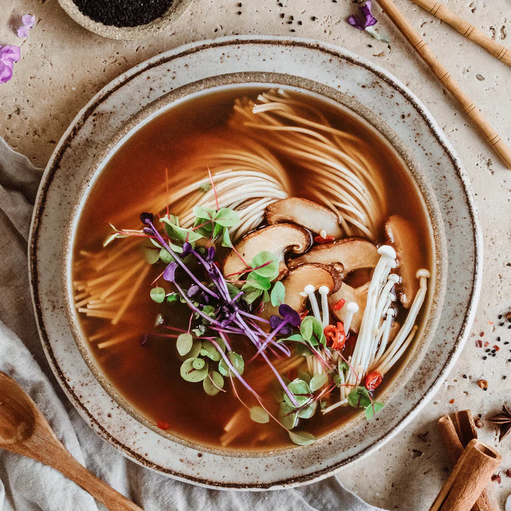 Noodle soup with mushrooms and herbs in a rustic bowl on a textured surface.