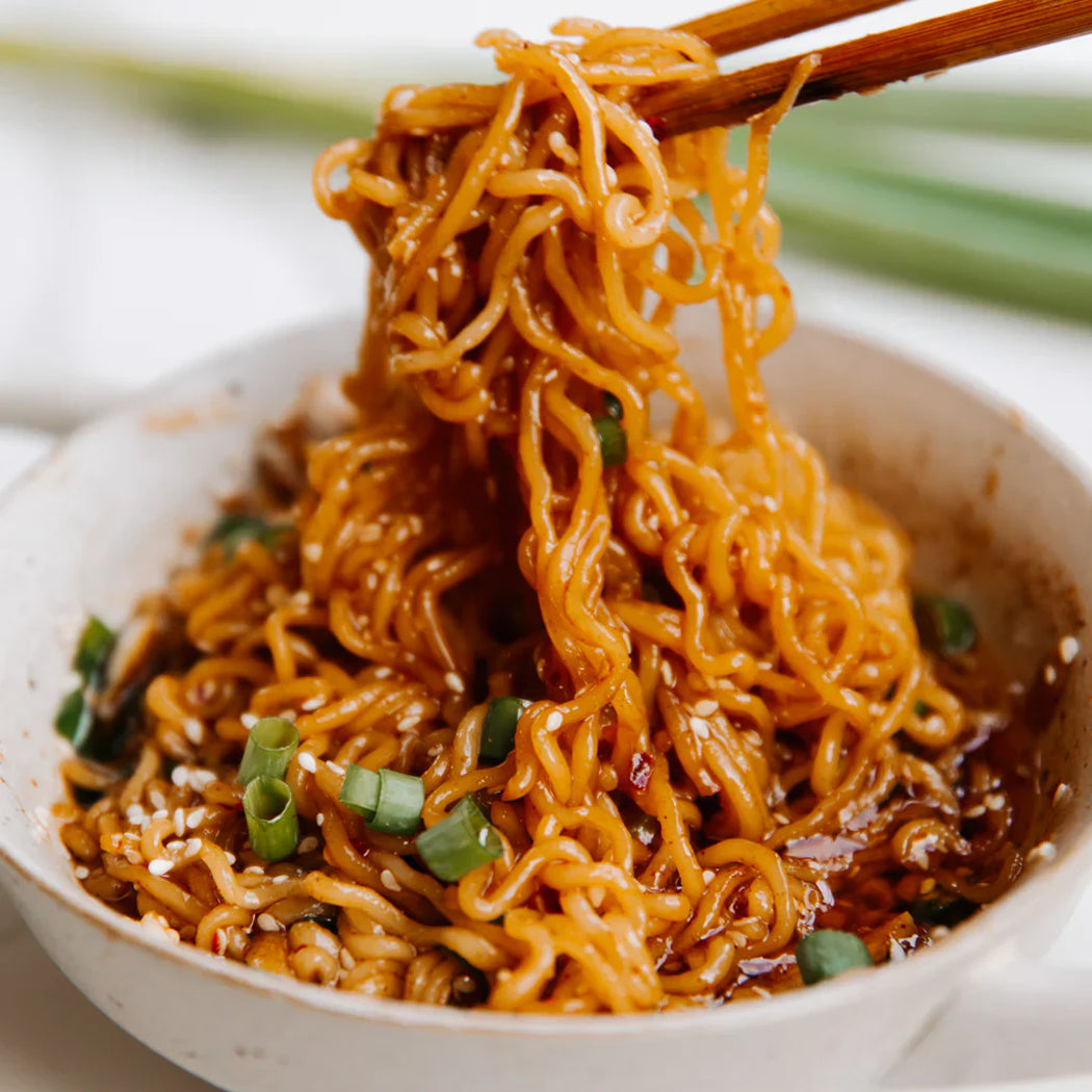 Noodles with chopsticks over a bowl of noodles on a white background