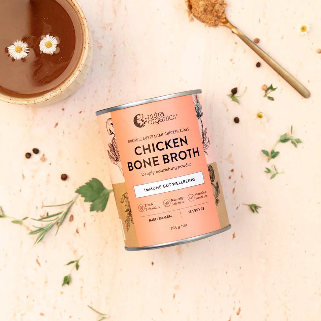 Can of Nutra Organics Chicken Bone Broth on a light background with herbs and a bowl.
