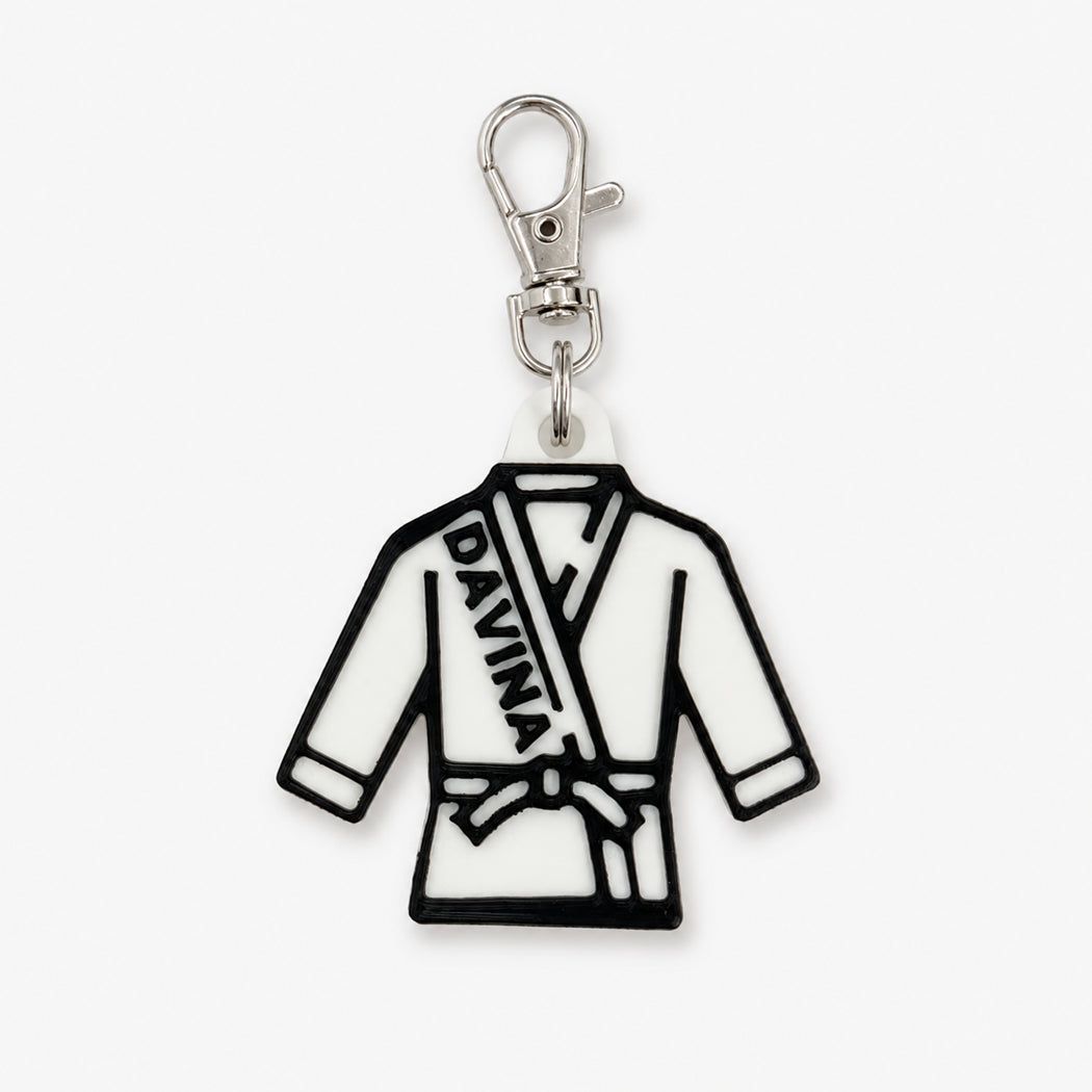 A white and black rubber charm shaped like a martial arts gi robe with the name 'DAVINA' printed on the chest, attached to a silver lobster clasp, shown on a light gray background.