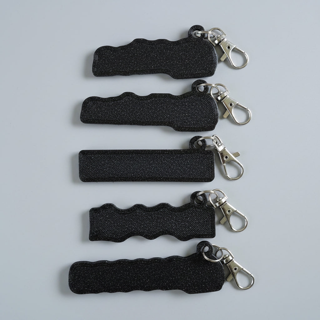 Five black textured keychains with silver metal clasp rings, arranged vertically on a light brown wood grain surface.