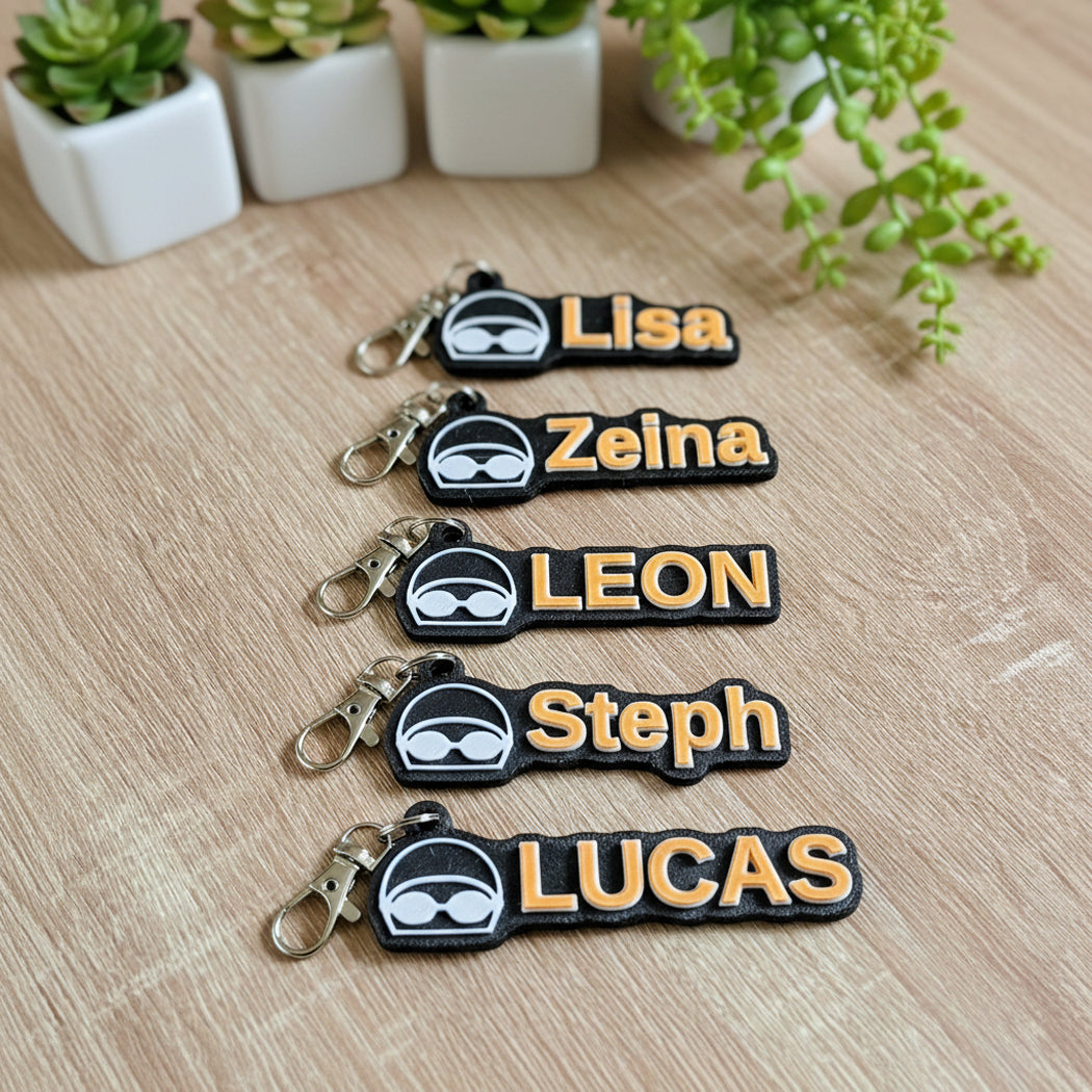 Five custom rubber keychains with black and gold names and a white ninja mask icon, arranged on a light wood surface with small potted plants in the background.