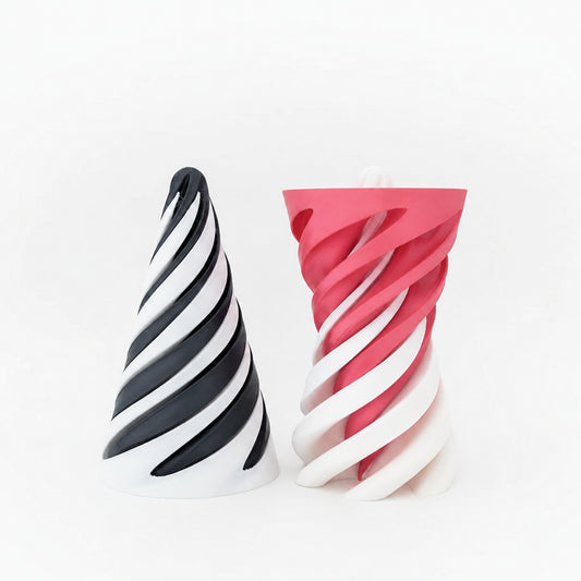 Two sculptural spiral cone-shaped objects on a clean white studio background. The left object has black and white diagonal stripes, and the right object is pink and white.