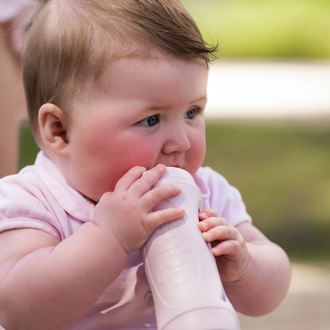 Baby in pink outfit holding a white object outdoors