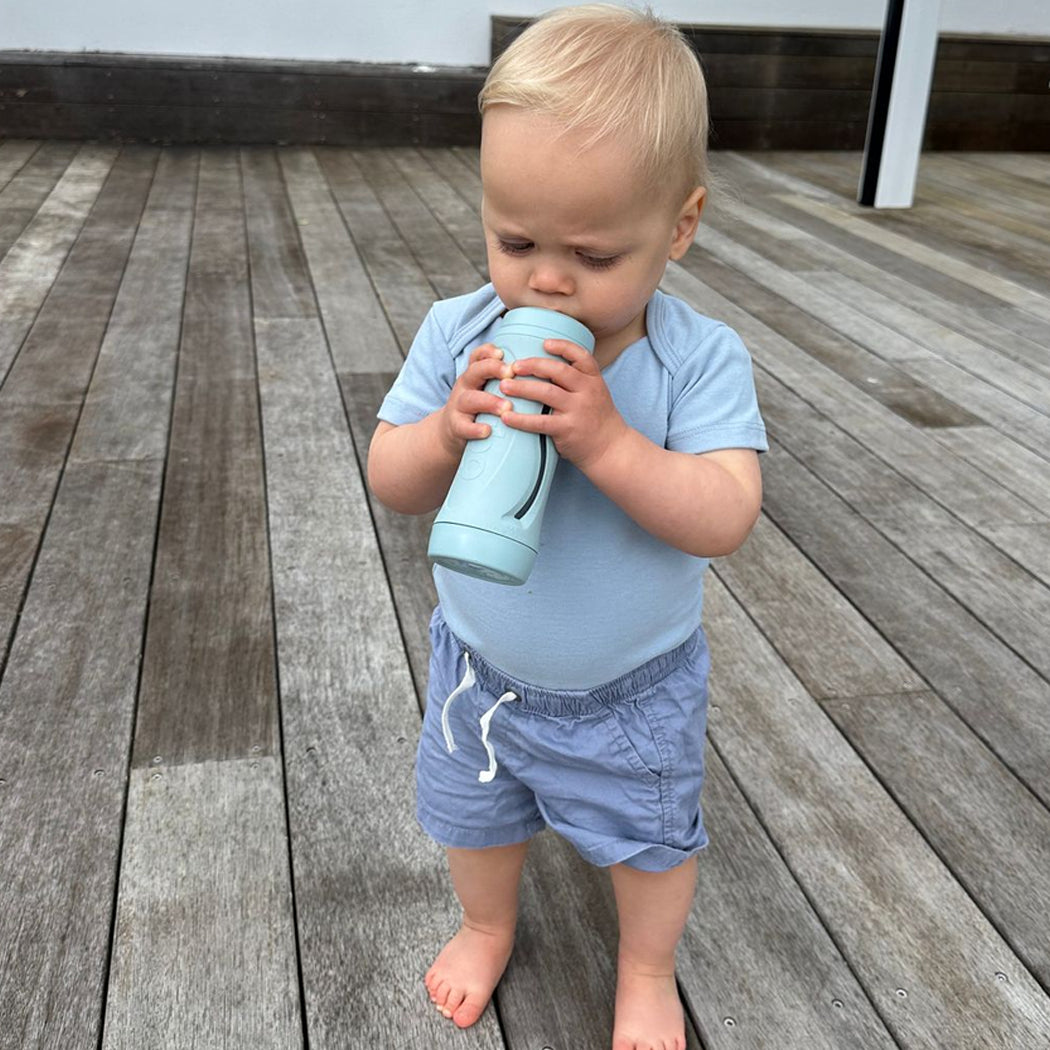 Child in blue outfit holding a blue bottle on a wooden deck