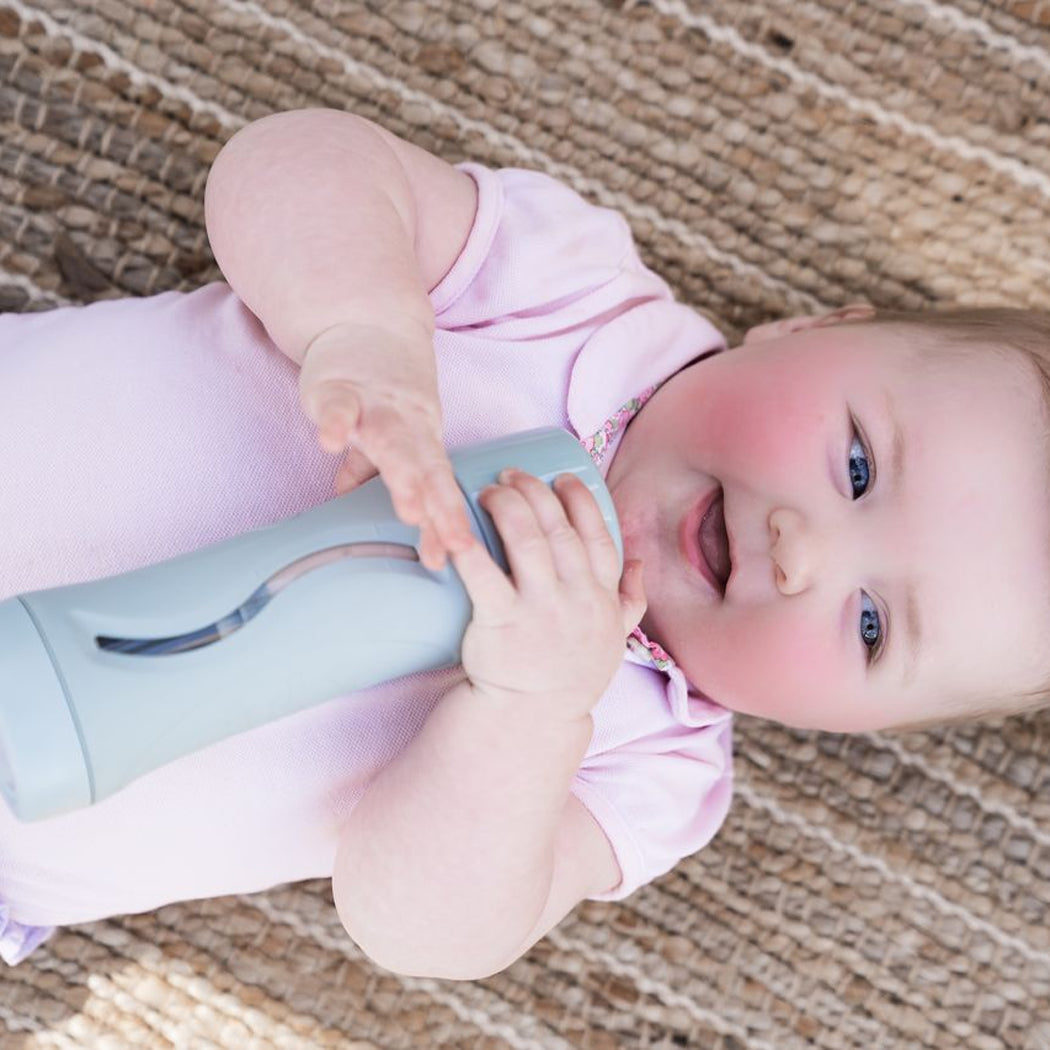 Baby lying on a textured surface holding a blue and gray toy.