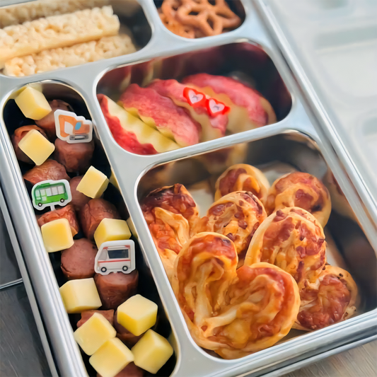 Metal bento box with compartments containing various snacks including cheese, fruit, and bread.