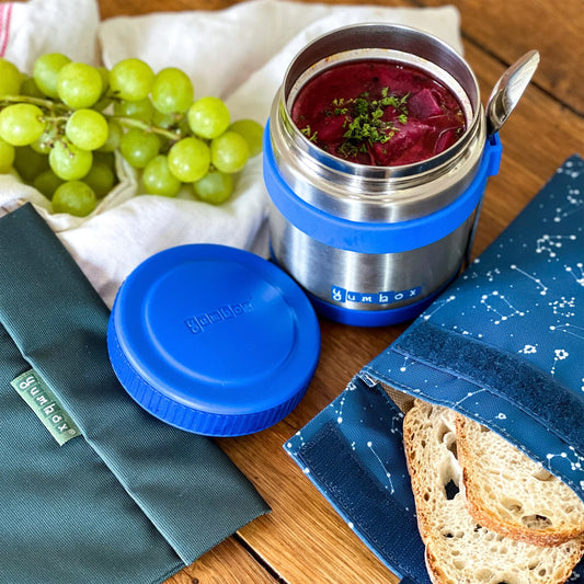 Stainless steel food container with blue lid, grapes, and bread on a wooden surface