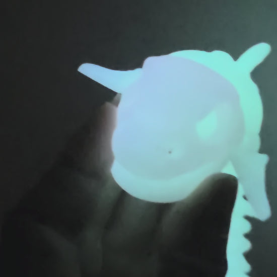 A glowing, bioluminescent-looking fish skeleton model or toy shown against a solid black background.