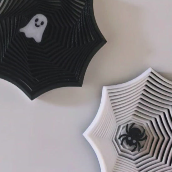 Two Halloween-themed fidgets on a light cream background. The left decoration is black with a white ghost in the center, and the right decoration is white with a black bat in the center.