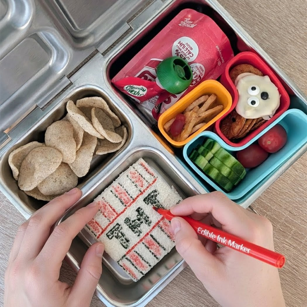 Bento box with compartments filled with snacks and a hand using an edible ink marker.